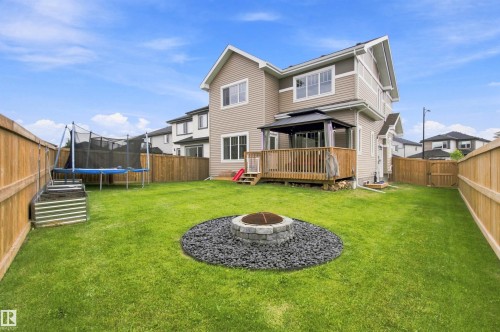 Expansive green lawn with a stone fire pit, wood fence, and a raised wood deck featuring a covered gazebo - 107 Ellice Bend, Fort Saskatchewan, AB 