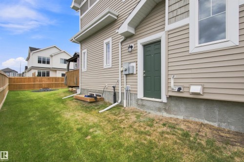 Rear exterior with beige siding, a dark green door, and a white-trimmed window - 107 Ellice Bend, Fort Saskatchewan, AB 