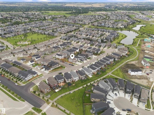 Aerial perspective showcasing a residential development with multiple detached homes, green spaces, and a nearby pond - 107 Ellice Bend, Fort Saskatchewan, AB 