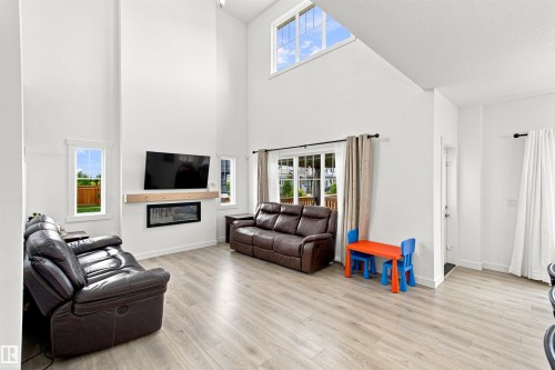 Soaring ceilings, light wood-finish flooring, and an integrated electric fireplace with a wood mantle - 107 Ellice Bend, Fort Saskatchewan, AB 