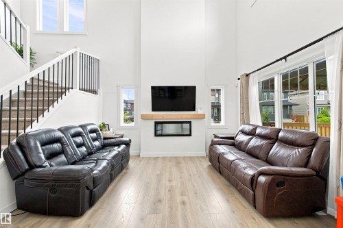 Two-story living area with high ceilings, light wood-finish flooring, and a contemporary linear fireplace - 107 Ellice Bend, Fort Saskatchewan, AB 