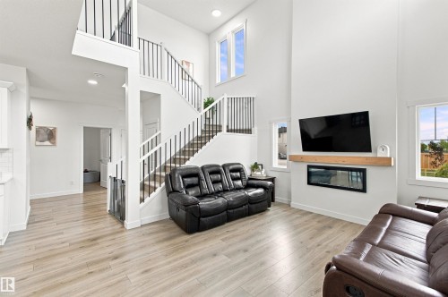 Two-story living area featuring a built-in linear fireplace with a wood-finish mantel, light wood-finish flooring, and a staircase with black metal balusters - 107 Ellice Bend, Fort Saskatchewan, AB 