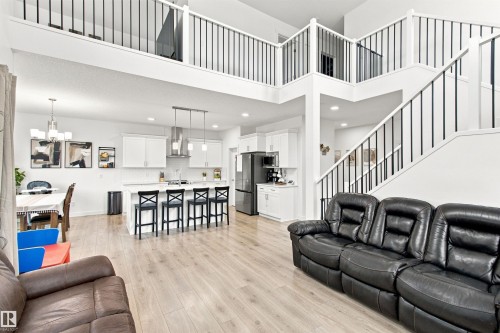 Open-concept living area featuring wood-finish flooring, a kitchen island with seating, white cabinetry, and a prominent staircase with black metal balusters - 107 Ellice Bend, Fort Saskatchewan, AB 