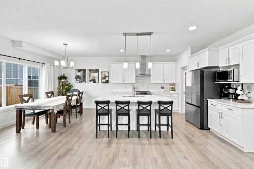Open-concept kitchen and dining area featuring light wood-finish flooring, white cabinetry, a large kitchen island with seating, and a modern stainless steel range hood - 107 Ellice Bend, Fort Saskatchewan, AB 
