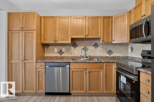 Kitchen featuring abundant wood-finish cabinetry, stainless steel appliances, a tile backsplash, and wood-finish flooring - #26 2816 34 Av Nw, Edmonton, AB 