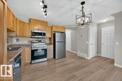 Kitchen featuring wood-finish cabinetry, stainless steel appliances, patterned tile backsplash, wood-look flooring, and a decorative chandelier - #26 2816 34 Av Nw, Edmonton, AB 