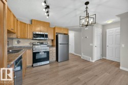 Kitchen featuring wood-finish cabinetry, stainless steel appliances, patterned tile backsplash, wood-look flooring, and a decorative chandelier - 