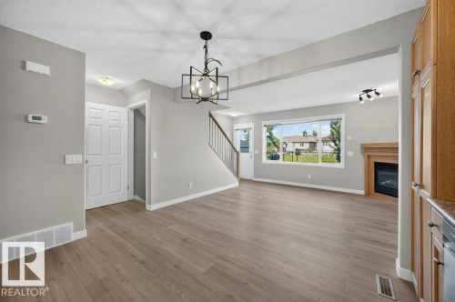 Open-concept living area with wood-finish flooring, a built-in fireplace featuring a wood mantel, and large picture windows - #26 2816 34 Av Nw, Edmonton, AB 