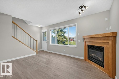 Wood-finish flooring, staircase with wood handrail and black spindles, built-in fireplace with wood mantel, large window, and track lighting fixture - #26 2816 34 Av Nw, Edmonton, AB 