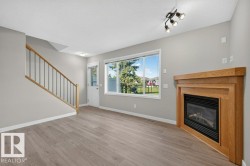 Wood-finish flooring, staircase with wood handrail and black spindles, built-in fireplace with wood mantel, large window, and track lighting fixture - 