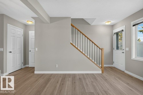 Wood-finish flooring throughout, light gray wall paint, white trim, white paneled doors, and a staircase with wood handrails and black metal spindles - #26 2816 34 Av Nw, Edmonton, AB 
