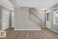 Wood-finish flooring throughout, light gray wall paint, white trim, white paneled doors, and a staircase with wood handrails and black metal spindles - 