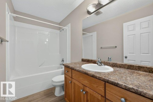 Bathroom featuring a white tub/shower combination, single vanity with a laminate countertop, wood-finish cabinetry, and a large wall mirror - #26 2816 34 Av Nw, Edmonton, AB 