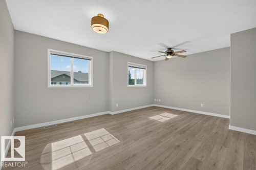 Spacious room with wood-finish flooring, two large windows, a ceiling fan, and a flush mount light fixture - #26 2816 34 Av Nw, Edmonton, AB 