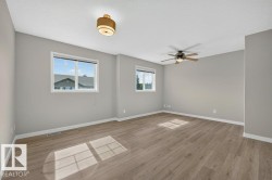 Spacious room with wood-finish flooring, two large windows, a ceiling fan, and a flush mount light fixture - 