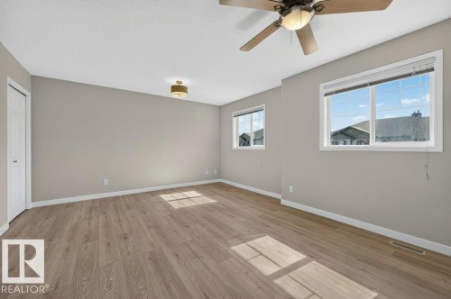 Wood-finish flooring, neutral wall paint, two large windows, a ceiling fan, and a flush-mount light fixture - #26 2816 34 Av Nw, Edmonton, AB 