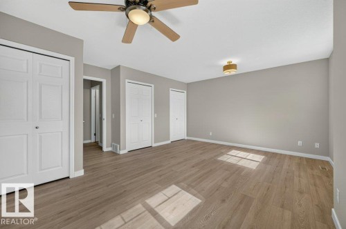 Wood-finish flooring, neutral wall tones, ceiling fan with integrated lighting, recessed ceiling light fixture, and multiple bi-fold closet doors - #26 2816 34 Av Nw, Edmonton, AB 