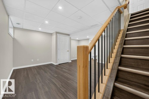 Finished lower level with wood-finish flooring, recessed lighting, and a white paneled door - #26 2816 34 Av Nw, Edmonton, AB 