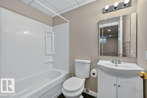 White built-in tub and shower unit, white vanity with integrated sink, chrome faucet, wall-mounted mirror, and vanity light fixture - #26 2816 34 Av Nw, Edmonton, AB 