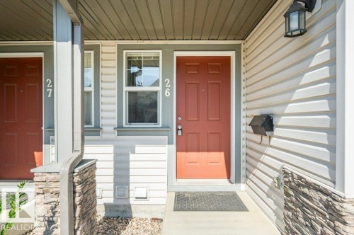 Entryway featuring a panel door, decorative outdoor lighting fixture, and stone veneer accents - #26 2816 34 Av Nw, Edmonton, AB 