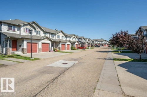 Row of townhomes featuring red garage doors, light-colored siding, and stone accents - #26 2816 34 Av Nw, Edmonton, AB 