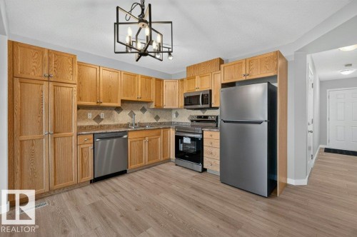 Kitchen featuring wood-finish cabinetry, stainless steel appliances, a mosaic tile backsplash, and wood-finish flooring - #26 2816 34 Av Nw, Edmonton, AB 