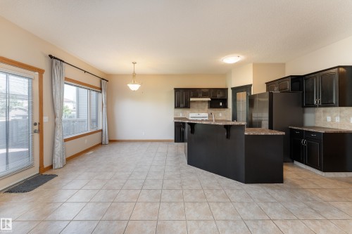 Spacious kitchen and dining area featuring tile flooring, dark wood cabinetry, light-colored countertops, a large kitchen island, and multiple windows - 10820 178 Avenue Nw, Edmonton, AB 