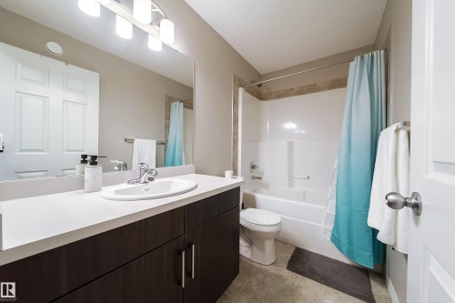 Dark wood-finish cabinetry with silver hardware, white countertop with integral sink, large vanity mirror, four-bulb vanity lighting fixture, and a combination tub and shower - 3211 Cherry Crescent Sw, Edmonton, AB 