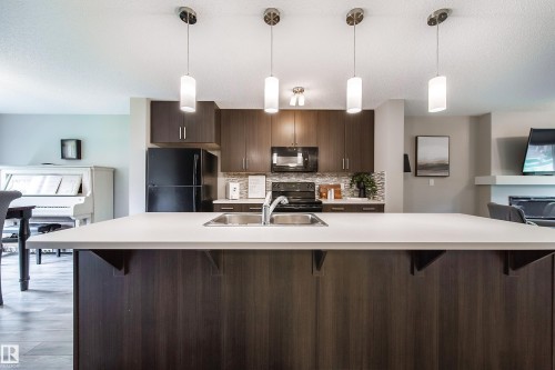 White countertop kitchen island with integrated stainless steel sink, dark wood-finish cabinetry, and stainless steel appliances - 3211 Cherry Crescent Sw, Edmonton, AB 