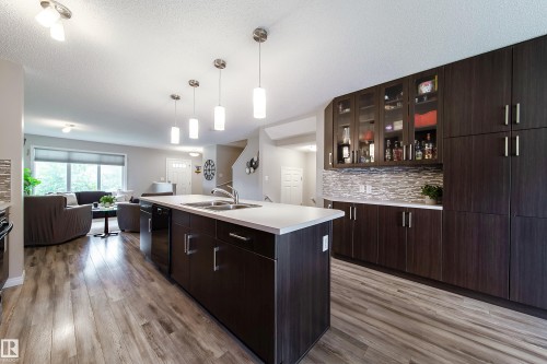 Kitchen featuring a central island with a double sink, dark wood-finish cabinetry, and a textured tile backsplash - 3211 Cherry Crescent Sw, Edmonton, AB 