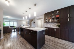 Kitchen featuring a central island with a double sink, dark wood-finish cabinetry, and a textured tile backsplash - 