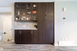Built-in cabinetry with glass-front uppers and solid lower doors, subway tile backsplash, light-toned countertop, and wood-finish flooring - 