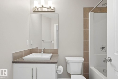 Modern bathroom featuring a rectangular vessel sink set on a dark countertop, white vanity cabinetry with brushed nickel hardware, and a tub/shower combination with tile surround - 206 Southfork Drive, Leduc, AB - Indoor Photo Showing Bathroom