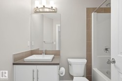 Modern bathroom featuring a rectangular vessel sink set on a dark countertop, white vanity cabinetry with brushed nickel hardware, and a tub/shower combination with tile surround - 