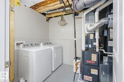Utility room featuring a white washer and dryer set, partially finished drywall, exposed ceiling joists with visible wiring and ductwork, and a Goodman furnace unit - 