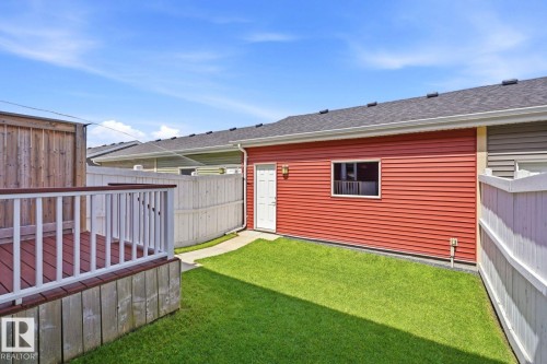 Private backyard featuring a raised wood deck with white railings, a vibrant green lawn, and a red-sided garage with a white entry door - 206 Southfork Drive, Leduc, AB - Outdoor With Exterior
