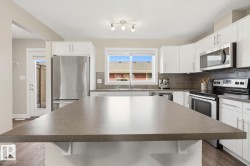 Kitchen featuring a large central island with a solid surface countertop, white cabinetry, stainless steel appliances, and wood-finish flooring - 