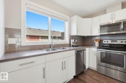 Modern kitchen featuring white cabinetry, dark countertops, a stainless steel double-basin sink, and a window with a white frame - 