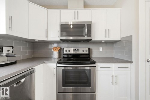 Contemporary kitchen featuring white cabinetry, stainless steel appliances, a grey subway tile backsplash, light grey countertops, and ample storage - 206 Southfork Drive, Leduc, AB - Indoor Photo Showing Kitchen With Stainless Steel Kitchen