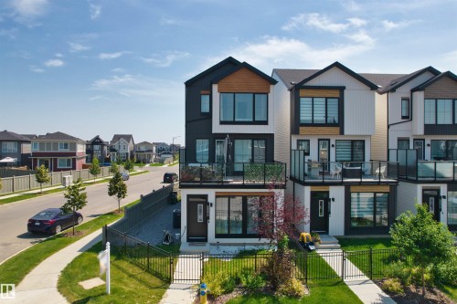 Modern townhome exterior with black frame windows, wood-finish accents, and a ground-level balcony featuring glass railings - 8047 227 Street Nw, Edmonton, AB 