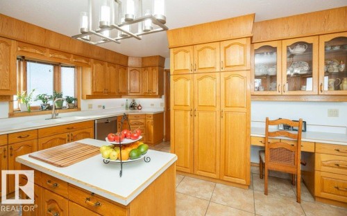Kitchen featuring extensive wood-finish cabinetry, tile flooring, a central island with a white countertop, and a built-in desk area - 11007 108 Avenue, Westlock, AB 