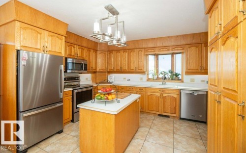 Kitchen featuring extensive wood cabinetry, stainless steel appliances, a central island, a double basin sink, and tiled flooring - 11007 108 Avenue, Westlock, AB 