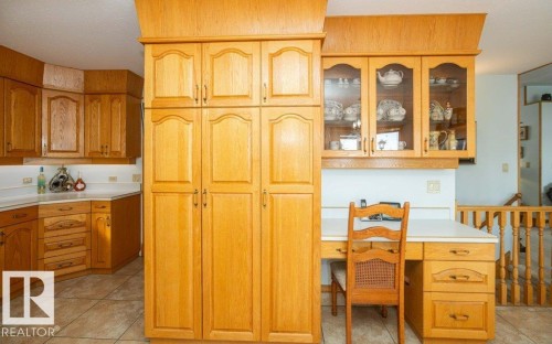 Extensive wood cabinetry, built-in desk, glass-front display cabinets, light-toned countertops, and tiled flooring - 11007 108 Avenue, Westlock, AB 