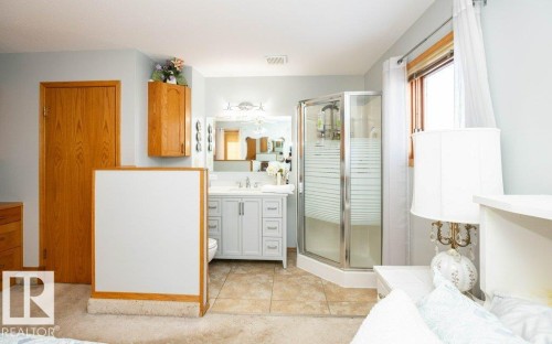 Integrated bathroom area featuring a single vanity with a white countertop, a mirrored medicine cabinet, a glass-enclosed corner shower, and tiled flooring - 11007 108 Avenue, Westlock, AB 