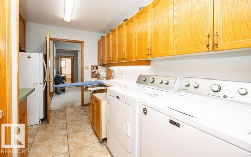 Laundry area featuring light wood cabinetry, tiled flooring, built-in appliances, and overhead fluorescent lighting - 11007 108 Avenue, Westlock, AB 