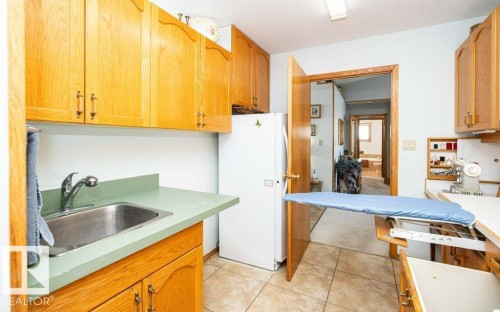 Light wood cabinetry, stainless steel sink, light green countertop, tile flooring, and a built-in ironing board - 11007 108 Avenue, Westlock, AB 