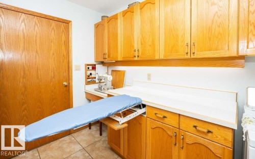Wood-finish cabinetry with brass hardware, white countertops, tile flooring, and a built-in ironing board - 11007 108 Avenue, Westlock, AB 