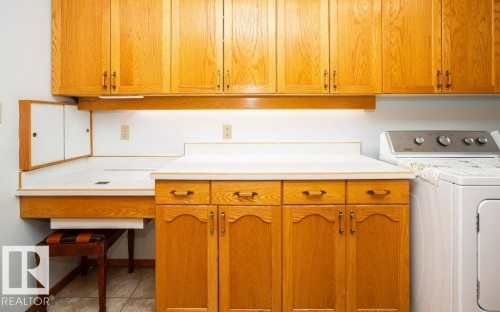 Wood-finish cabinetry with brass hardware, white countertops, built-in desk area, and ceramic tile flooring - 11007 108 Avenue, Westlock, AB 