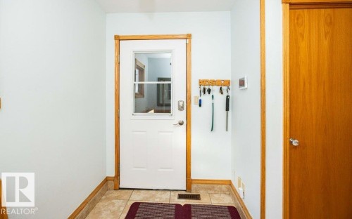 Welcoming entryway featuring wood-trimmed doorways, ceramic tile flooring, and organized wall-mounted storage hooks - 11007 108 Avenue, Westlock, AB 
