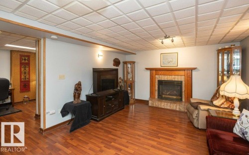 Fireplace with wood mantel and brick surround, wood-finish flooring, and drop ceiling with recessed lighting - 11007 108 Avenue, Westlock, AB 